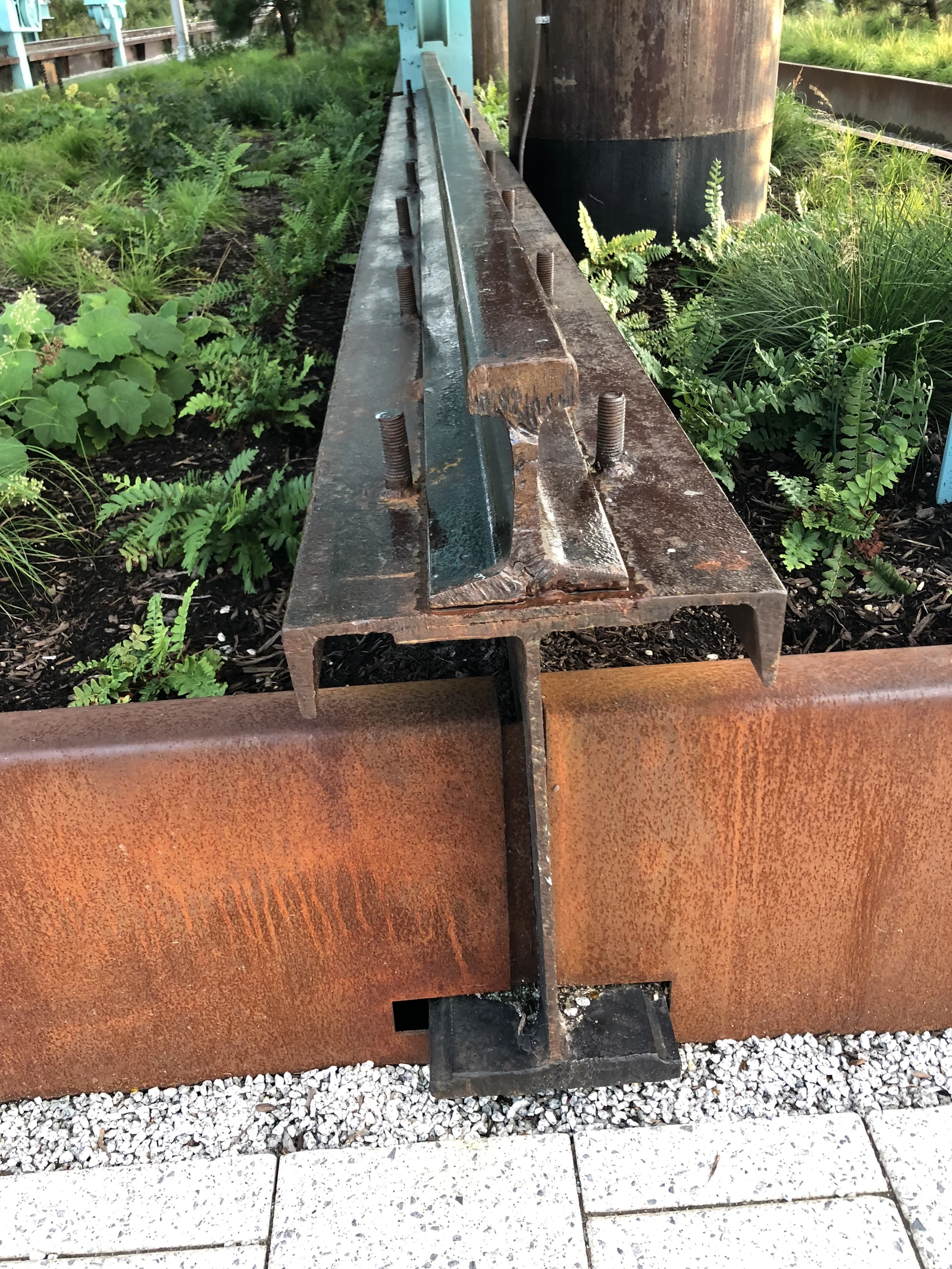 Weathered steel beams, exposed bolts and a cylindrical industrial artifact meet green planting at Domino Park.