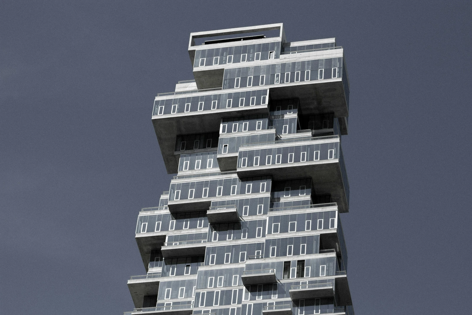 Stacked glass volumes and deep cantilevered terraces at 56 Leonard Street against a slate-blue sky.