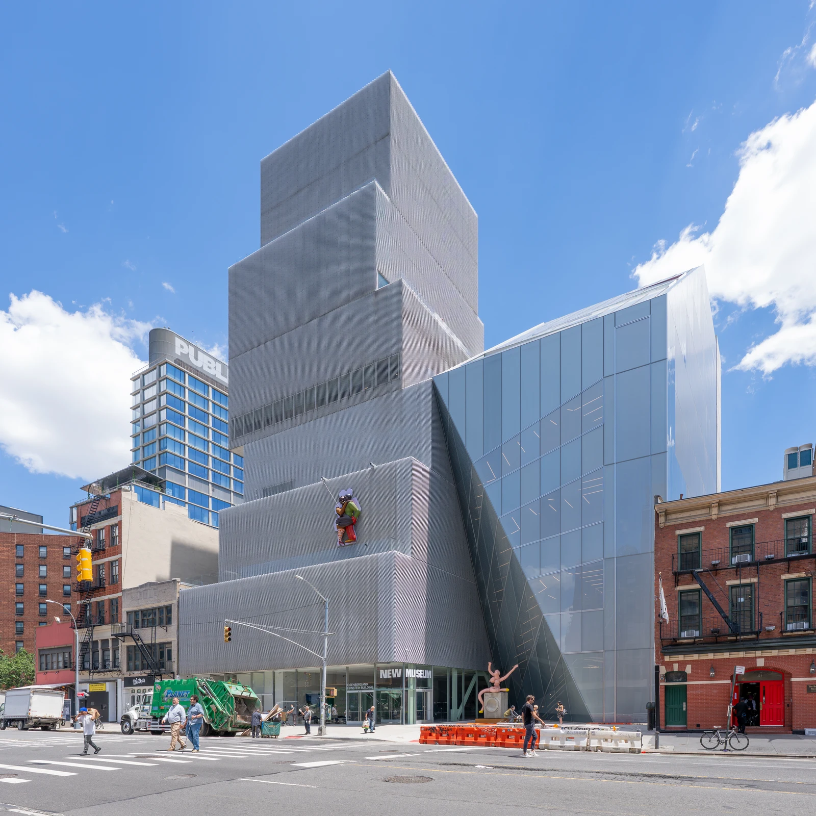 The New Museum on the Bowery: stacked silver mesh volumes beside an angular glass expansion, with red-brick neighboring buildings under a blue sky.